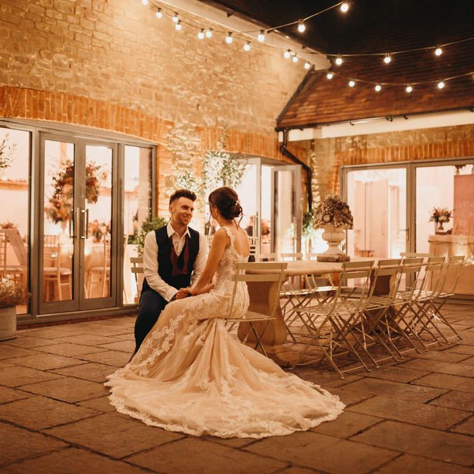 Bride and groom sitting outside Millbridge Court at evening reception with fairy lights 