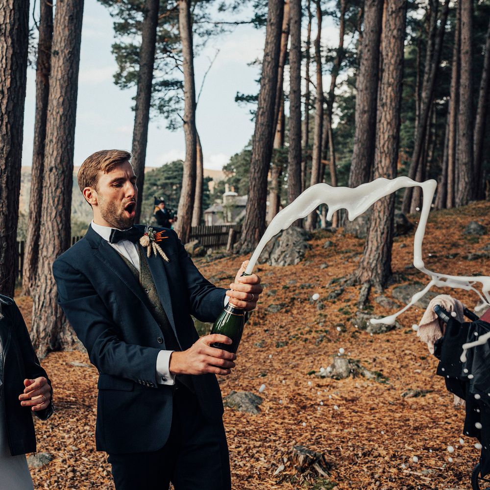 Groom pops champagne outdoors with bride on wedding day