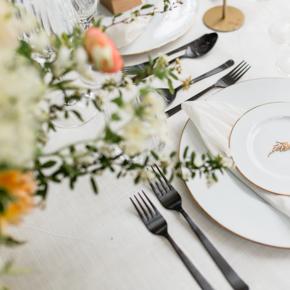 Elegant place setting with gold rimmed white plates and a gold broach decor 