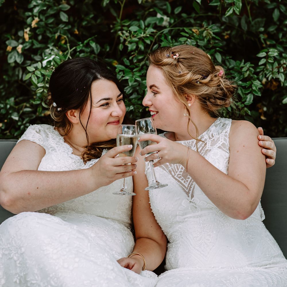 Brides look lovingly at one another on their wedding day as they cheers with champagne in flute glasses