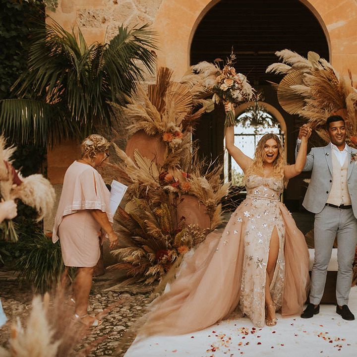 Bride raises her hands in celebration as she walks with groom on her wedding day