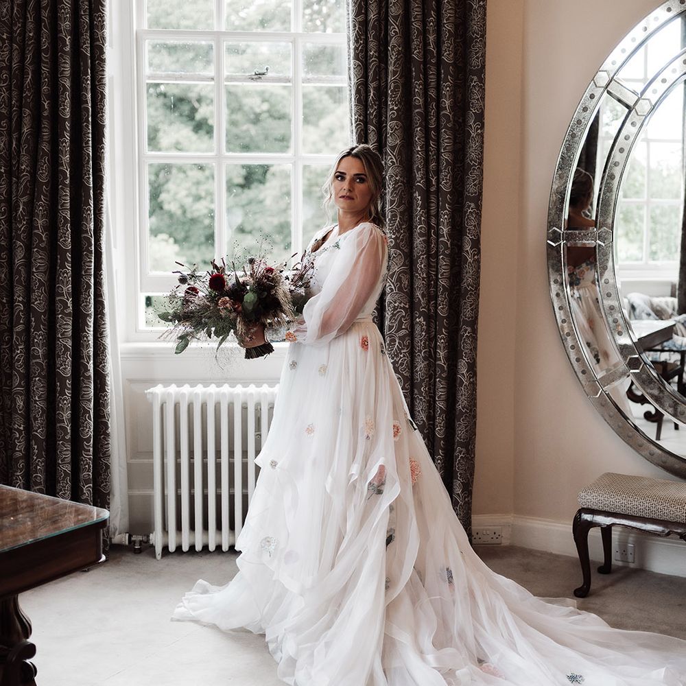 Bride in a Victoria Sanders embroidered wedding dress holding her dried and fresh flower bouquet by the window at Iscoyd Park 