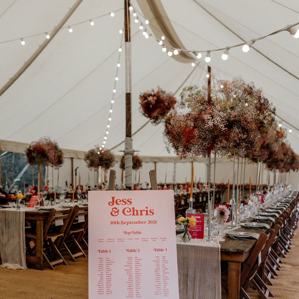 Marquee wedding reception with pink gypsophila flower clouds, festoon lights and a contemporary pink seating chart 