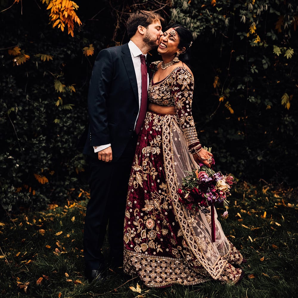 Grooms matches bride in his burgundy tie and dark suit as Bride wears Gold & Burgundy Indian saree wedding dress 