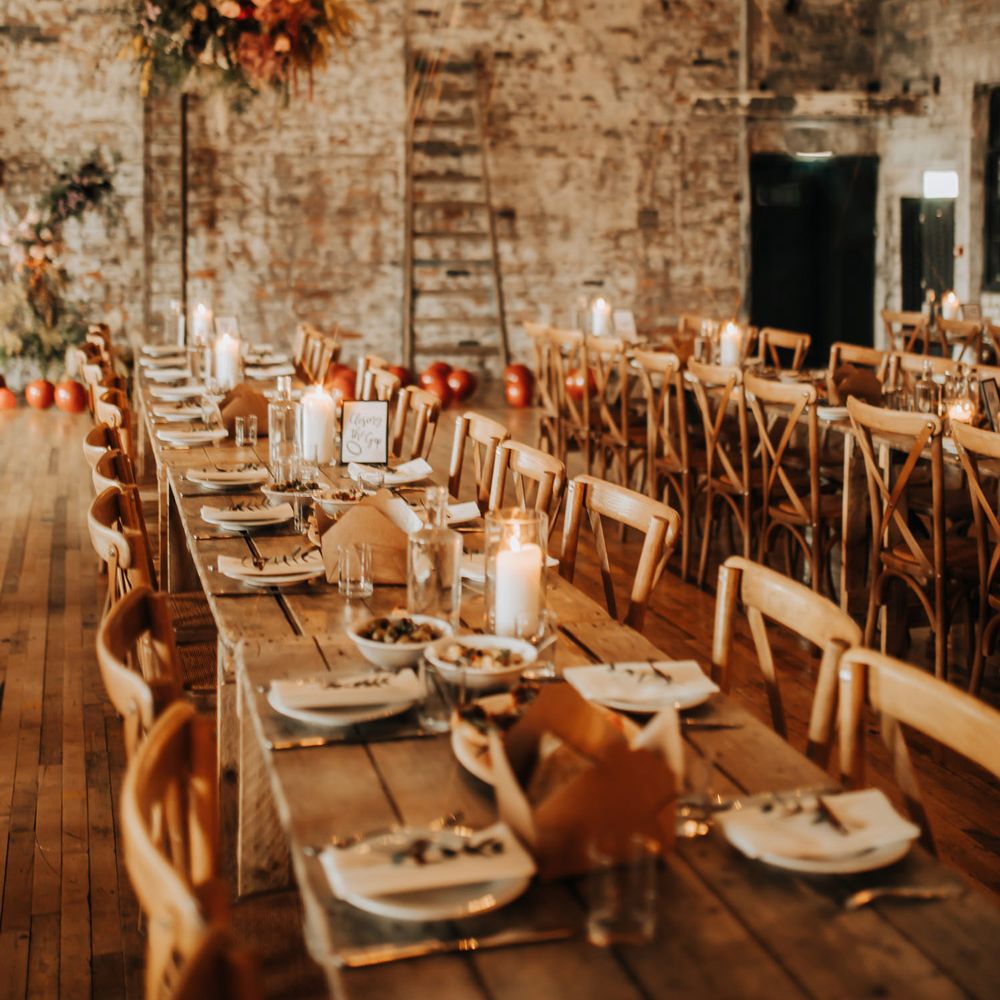 Long wooden tables and chairs in industrial style wedding reception room with exposed brick, bulb string lights and flower cloud for city centre wedding