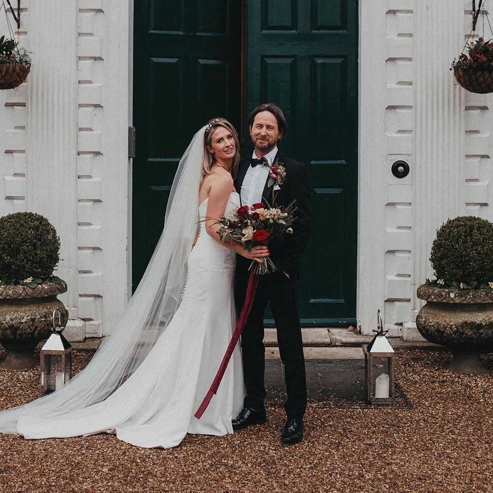 Bride & groom stand in front of green door on their wedding day as bride wears Helen Martin Veil and Suzanne Neville wedding gown