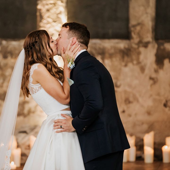Groom in navy blue suit and bride in wedding skirt and top share a kiss