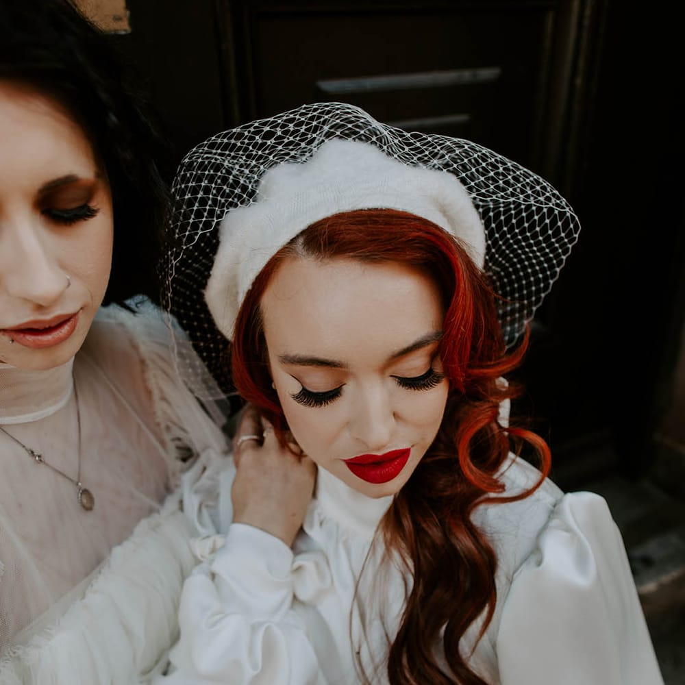 Bride in a high neck wedding dress with long sleeves wearing a berret with birdcage veil, red lipstick and false eyelashes 