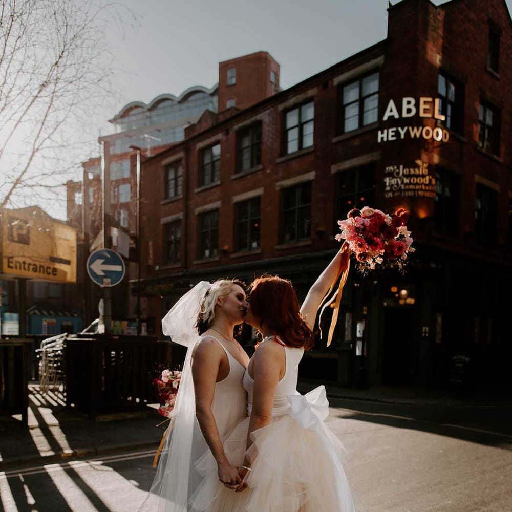 Manchester elopement with two brides kissing in a layered tulle skirt wedding dress and satin slip wedding dress with long bow veil 