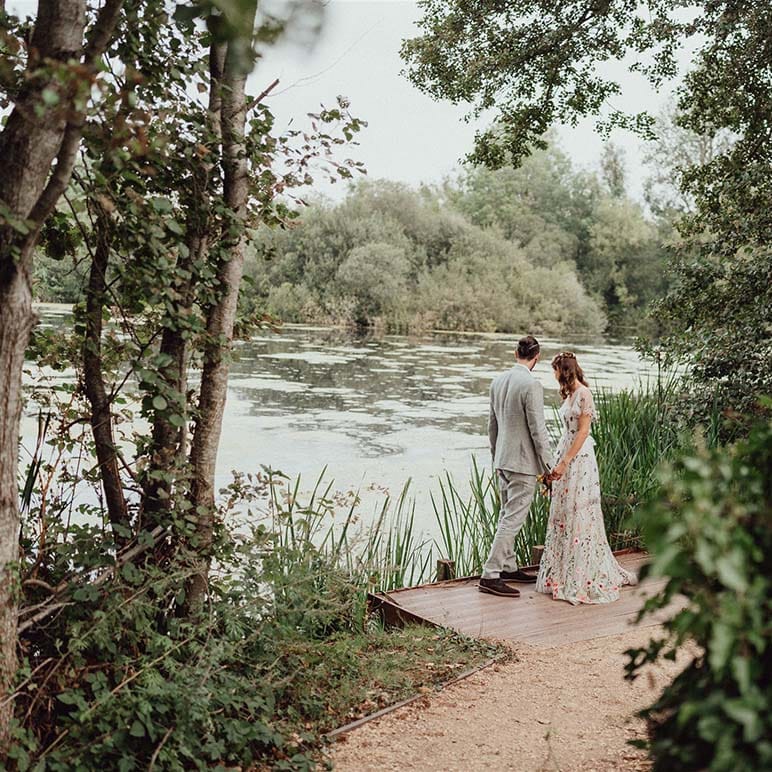 Bride in floral embroidered wedding dress with groom in grey suit looking out over the lake