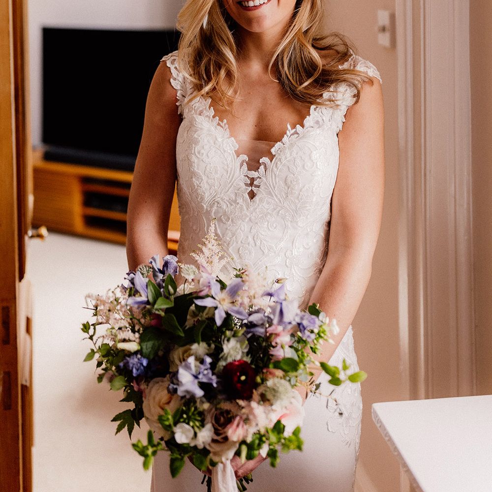 Bride in classic lace wedding dress with pink and purple bouquet with pearl drop earrings and pearl headpiece 
