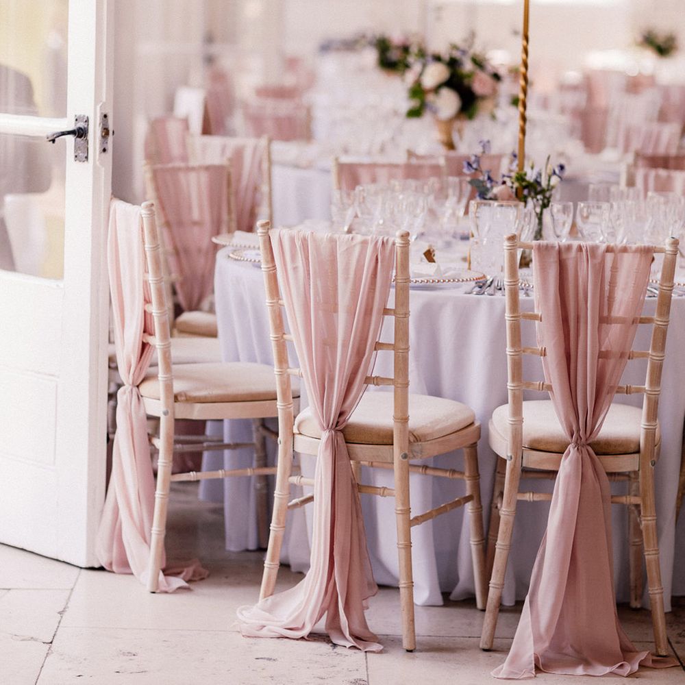 White wooden wedding chairs decorated with pink chiffon material with tables decorated with tall pink rose centrepieces 