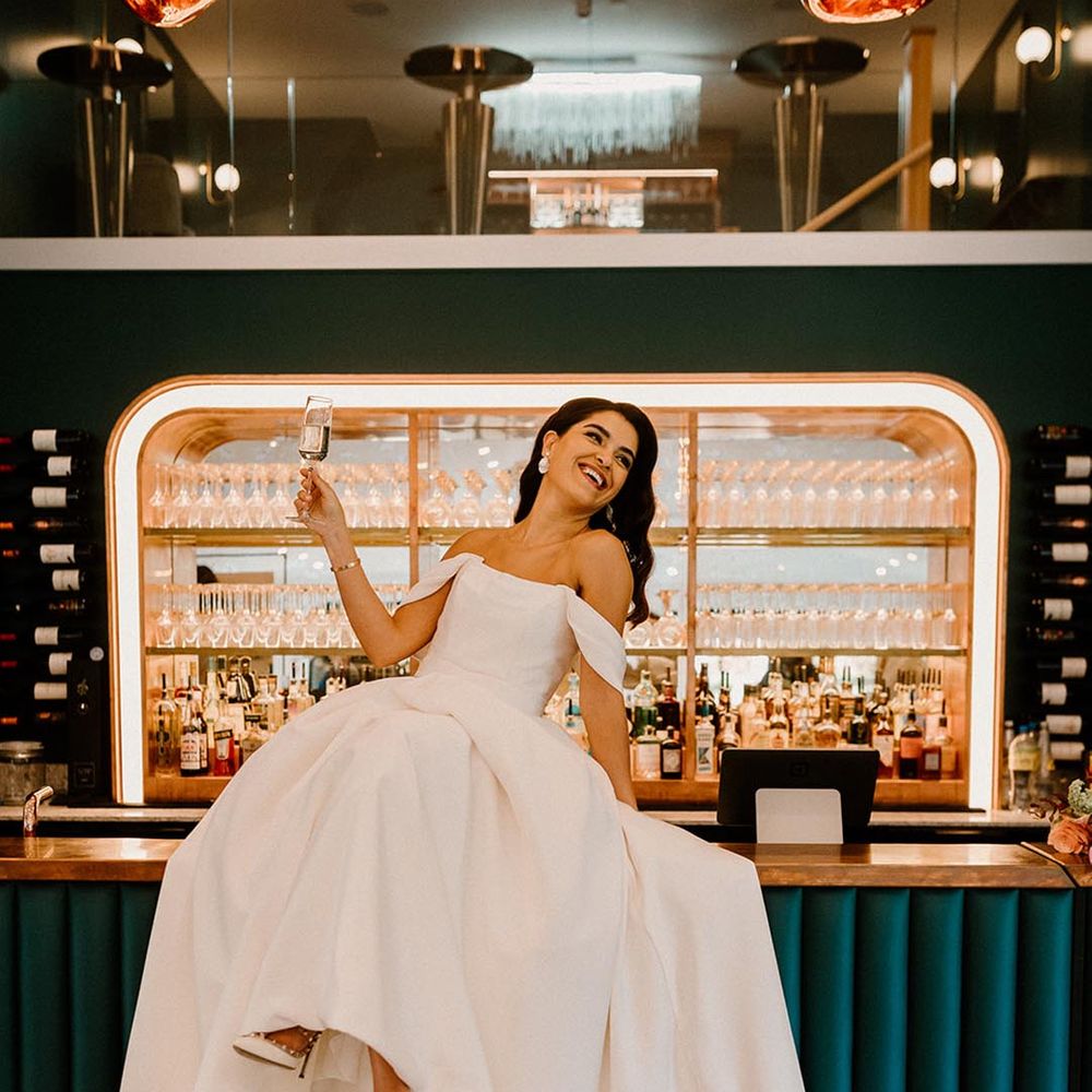 Bride lounges back on the bar with a glass of champagne in her hand