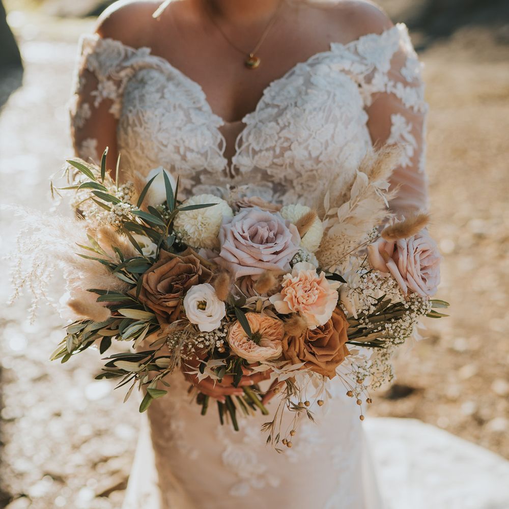 Bride wearing off the shoulder lace wedding dress holds pastel floral bouquet 