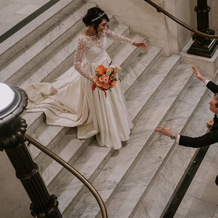 Groom running toward bride with open arms, bride wearing taffeta material princess wedding dress with long lace sleeves 