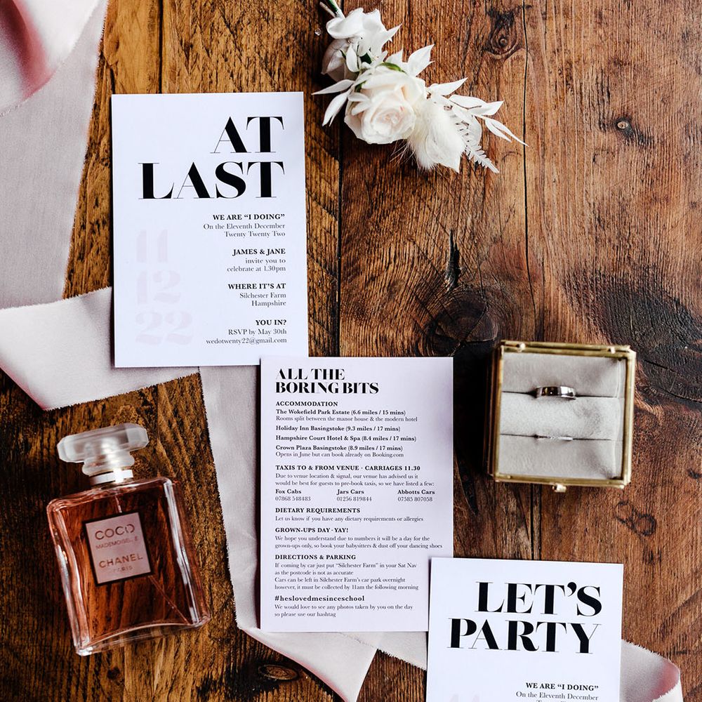 Black and white wedding stationery with Chanel perfume, pink ribbon, the wedding rings, and a buttonhole flower accessory 