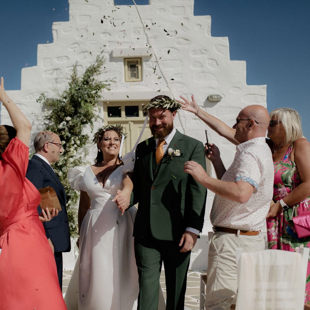 Bride and groom smiling during their confetti exit from intimate wedding ceremony in Paros, Greece