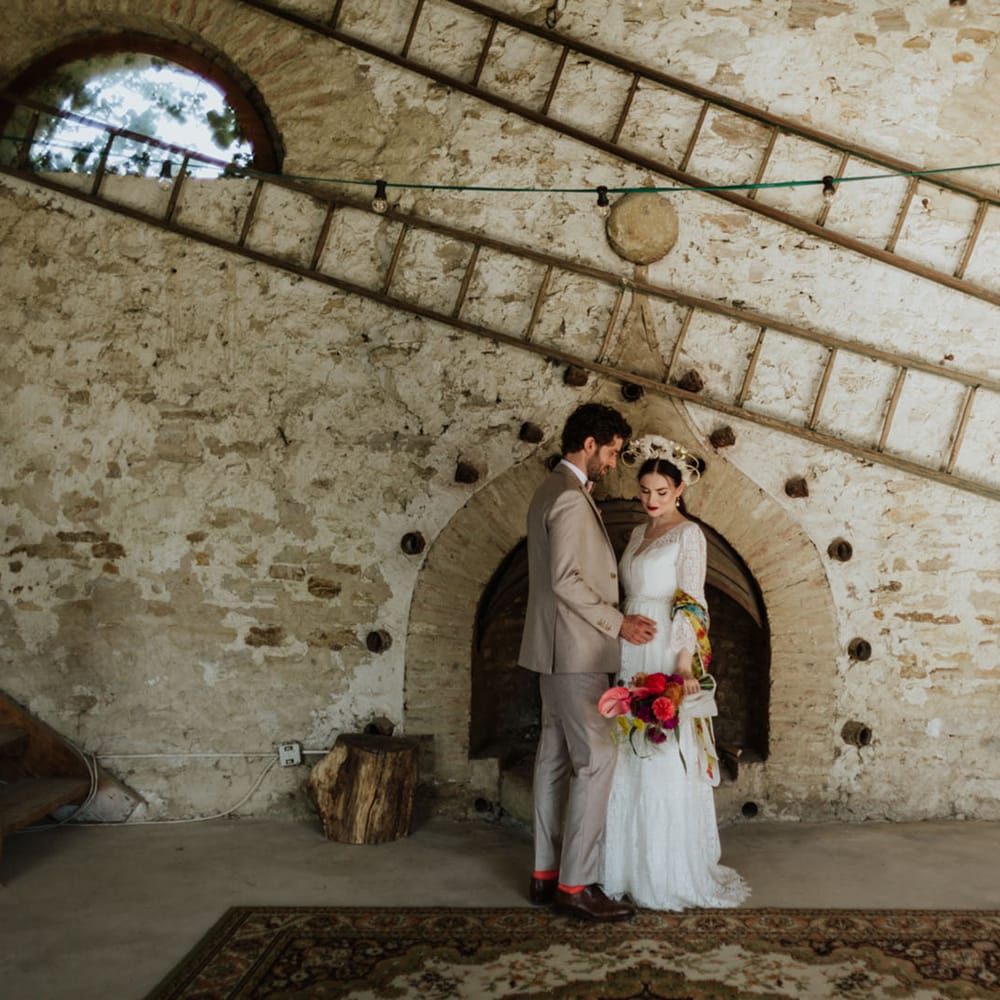 Bride and groom at rustic wedding venue in italy wearing a white lace wedding dress, boho bridal crown, and greige groom's suit