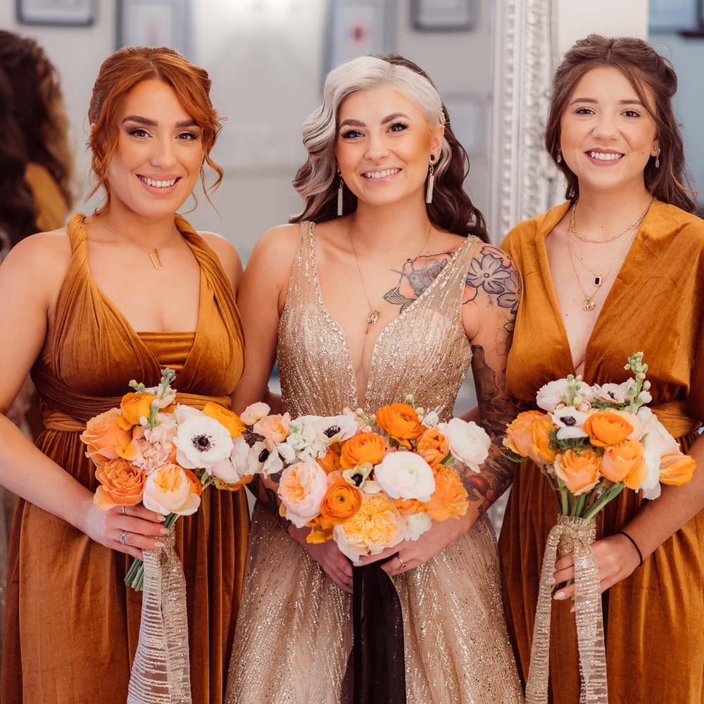 Bridal party wearing burnt orange velvet bridesmaid dresses holding orange and yellow wedding bouquets 