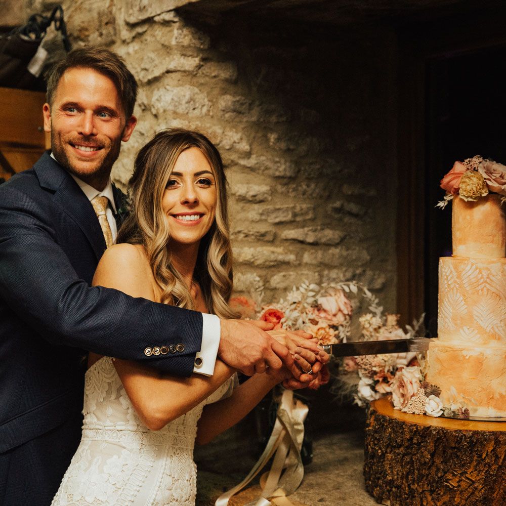 Smiling bride and groom cut three tiered dusty pink cake with rose flower decoration 
