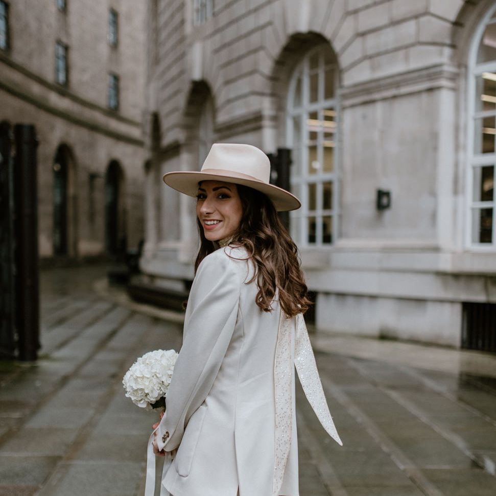Bride with long brown wavy hair in a fedora hat at intimate city wedding 