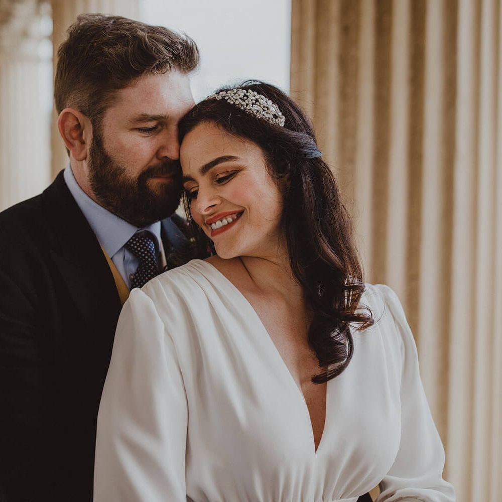 Bride and groom kissing bride wears diamante hair accessory and groom wears navy suit jacket, blue shirt and polka tie