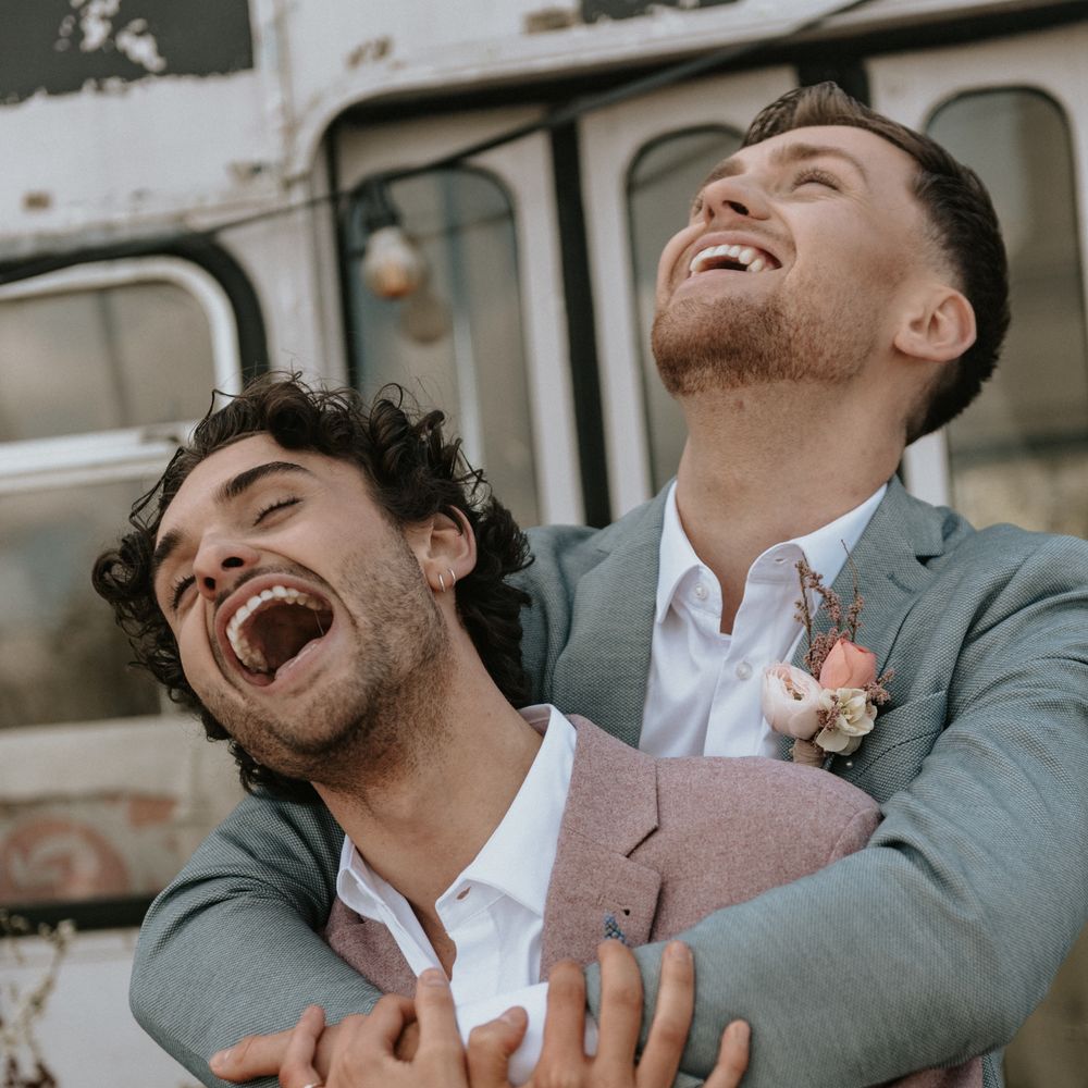 Grooms laugh with one another outdoors whilst wearing pastel suits