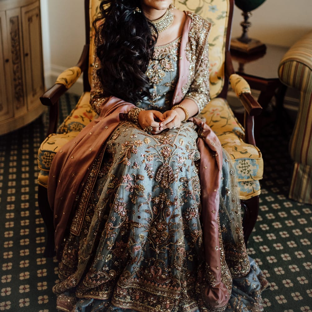 Bride sits on chair as she wears traditional saree and her dark hair in loose curls