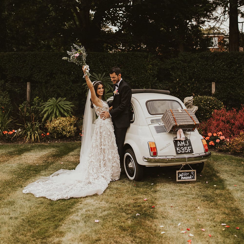 Bride & groom celebrate as bride puts her arm in the air whilst holding her bridal bouquet