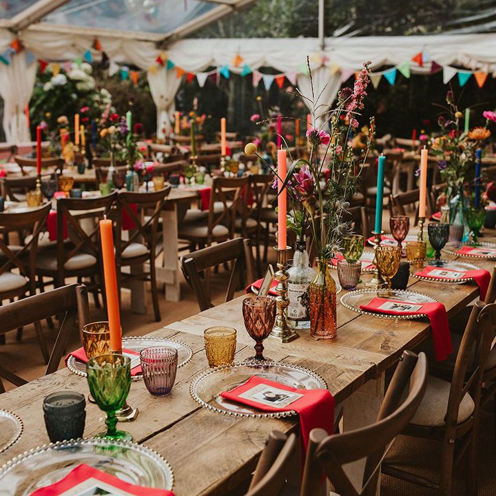 Vibrant wedding table decor with coloured goblets, napkins, flowers and candles in a clear marquee 