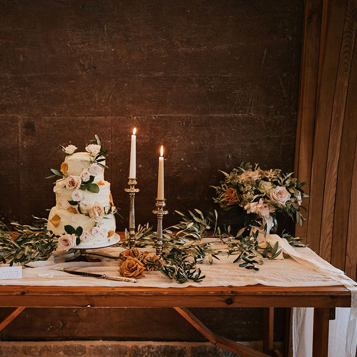 Buttercream wedding cake decorated with flowers on a cake table with candlesticks and floral arrangements 