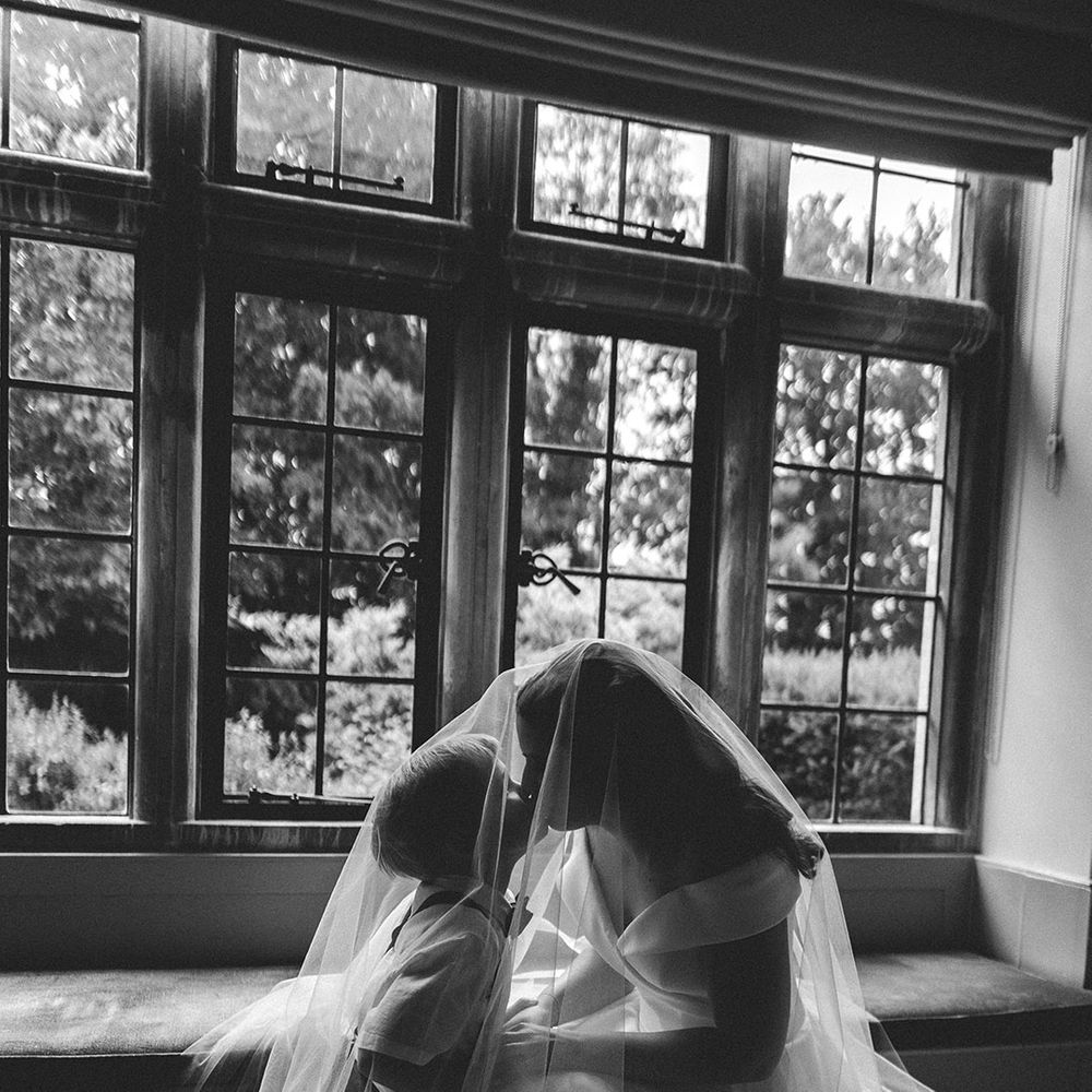 Bride in an off the shoulder Suzanne Neville wedding dress kissing her son under her wedding veil on the wedding morning 