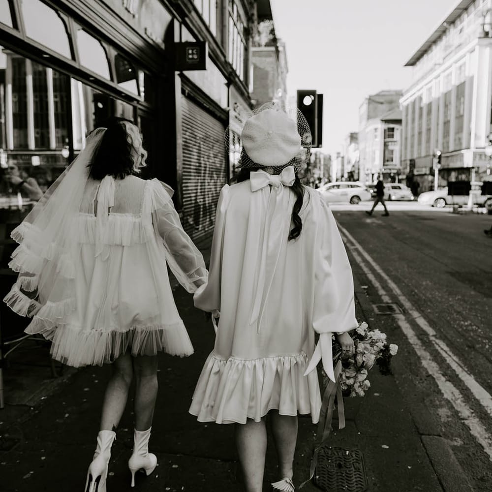 Manchester elopement with two brides in short wedding dresses with a long veil and berret hat holding hands 