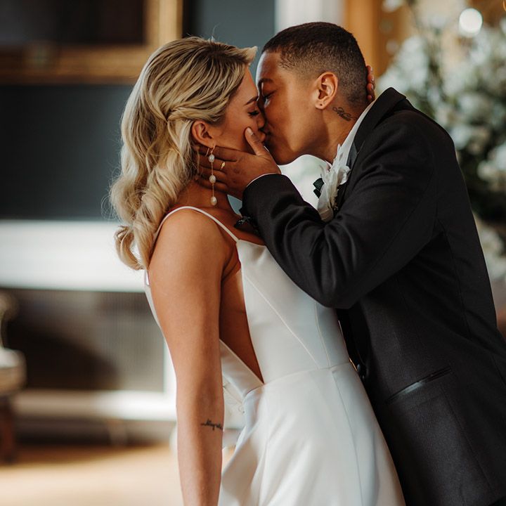 LGBTQI+ couple kissing at luxe Hodsock Priory wedding with the bride wearing a princess wedding dress with sheer side panel 