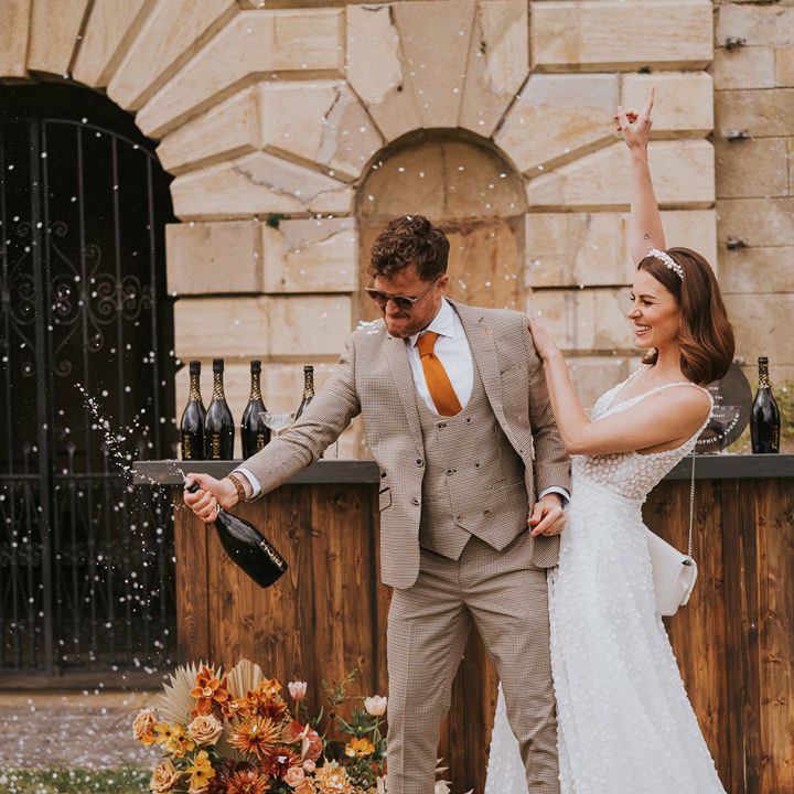 Couple in white headband and lace sleeveless dress and tartan suit popping champagne