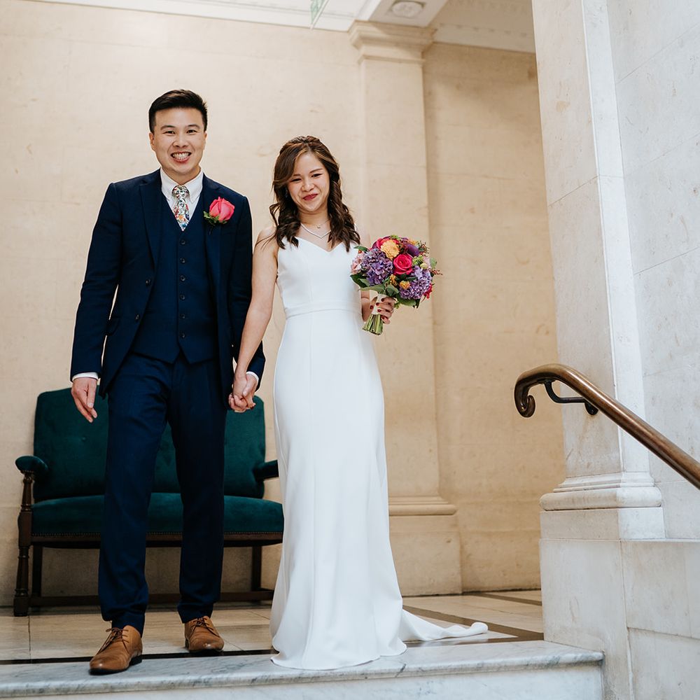 Bride wears elegant and classic white wedding dress whilst holding brightly coloured floral bouquet 