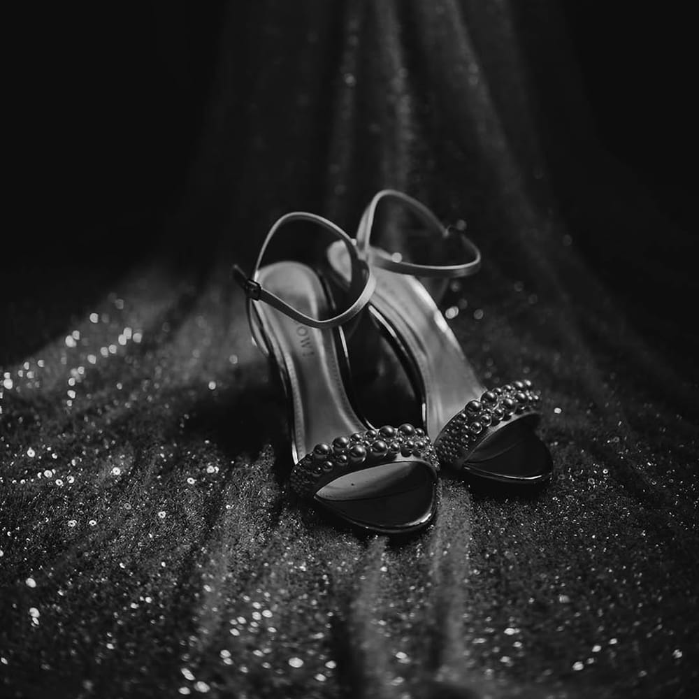 The bride's metallic wedding shoes with pearl details on the strap rest on the beaded train of her wedding dress
