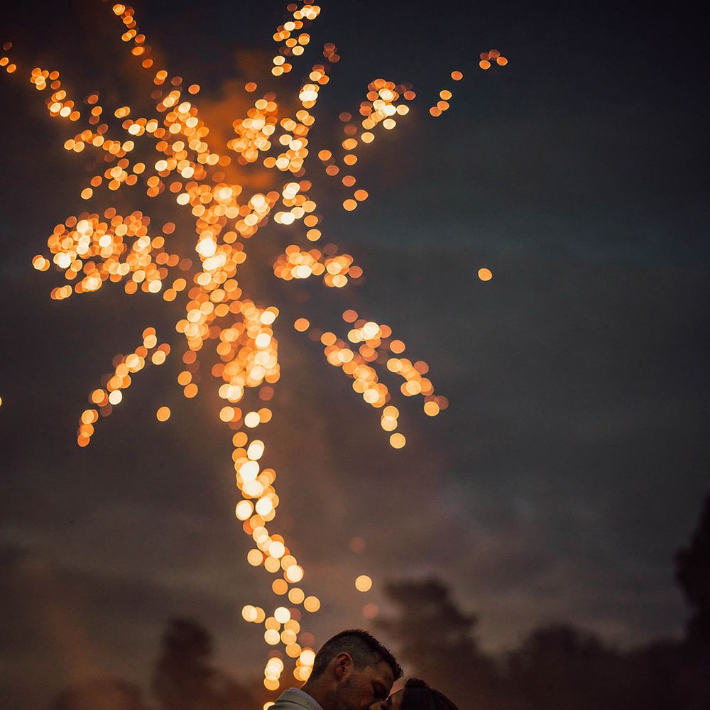Bride and groom share a kiss as fireworks go off in the background 