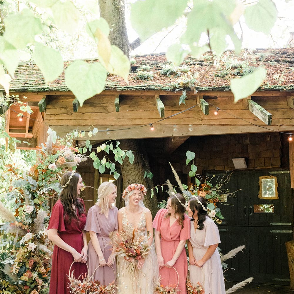 Bride stands with her bridesmaids in Rewritten Bridesmaid dresses in mismatched colours 