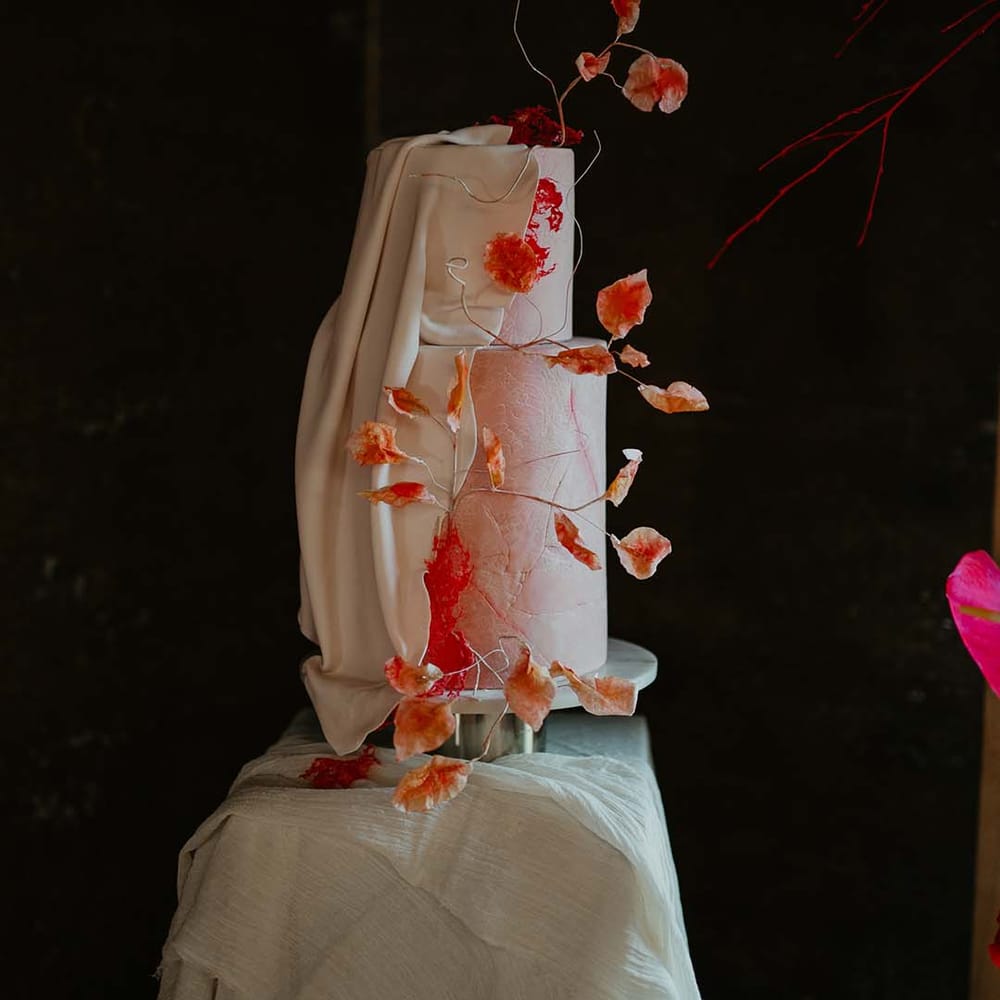 Two tier buttercream wedding cake with orange and magenta sugar flower decorations and large icing cover