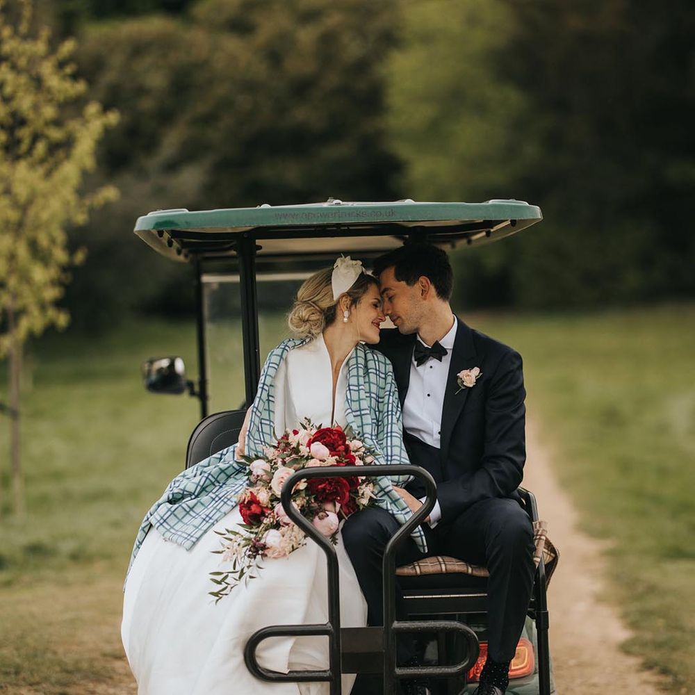 The bride rests against the groom with a blanket wrapped around her on a golf buggy that takes the couple around the venue 