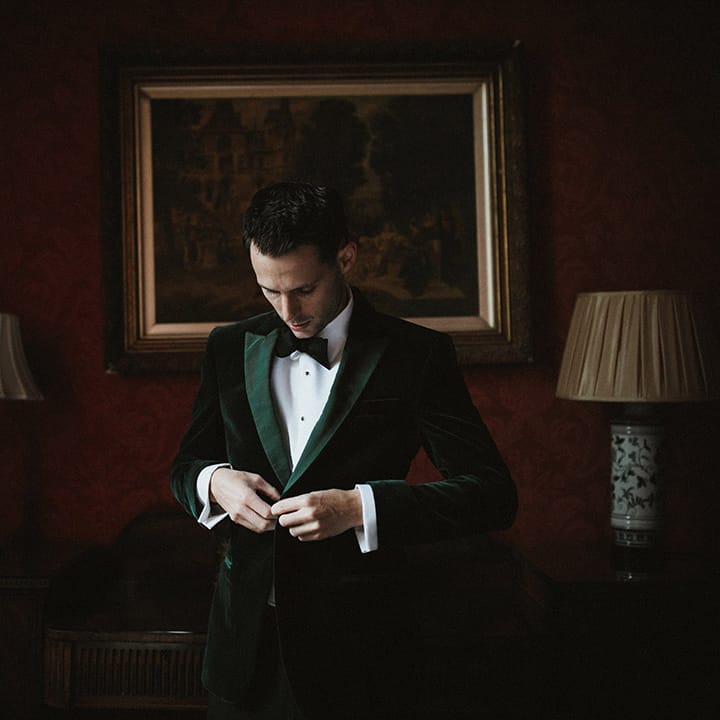 The groom in a velvet green tuxedo with a black bow tie gets ready for the wedding 