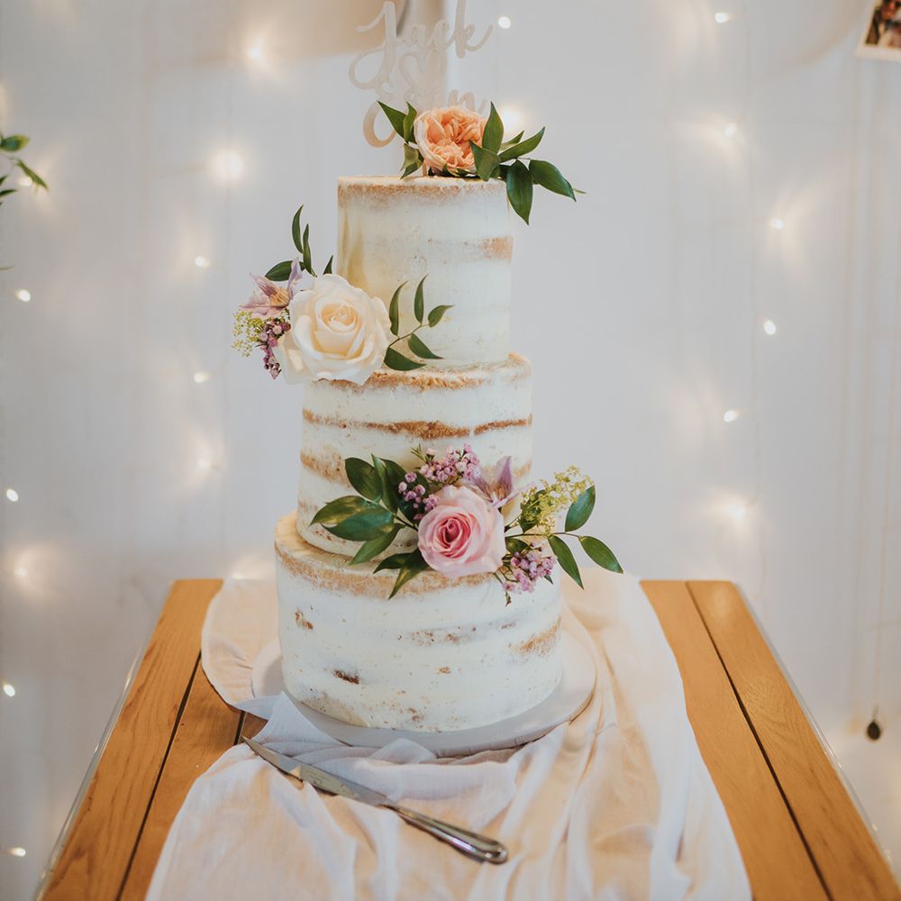 Rustic three tier semi-naked wedding cake with white icing with pastel roses and custom white cake topper 
