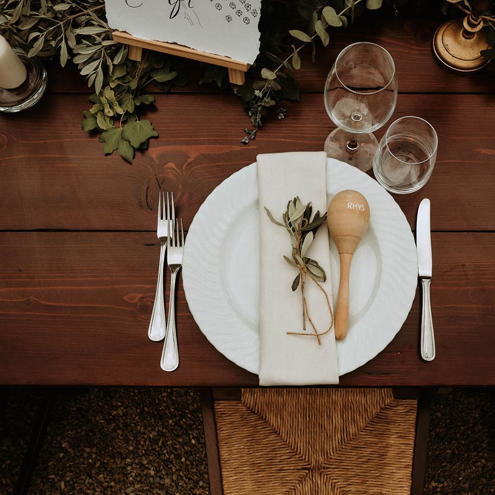 Wooden table setting with white napkins, ecaluptus, candles and maraca favours