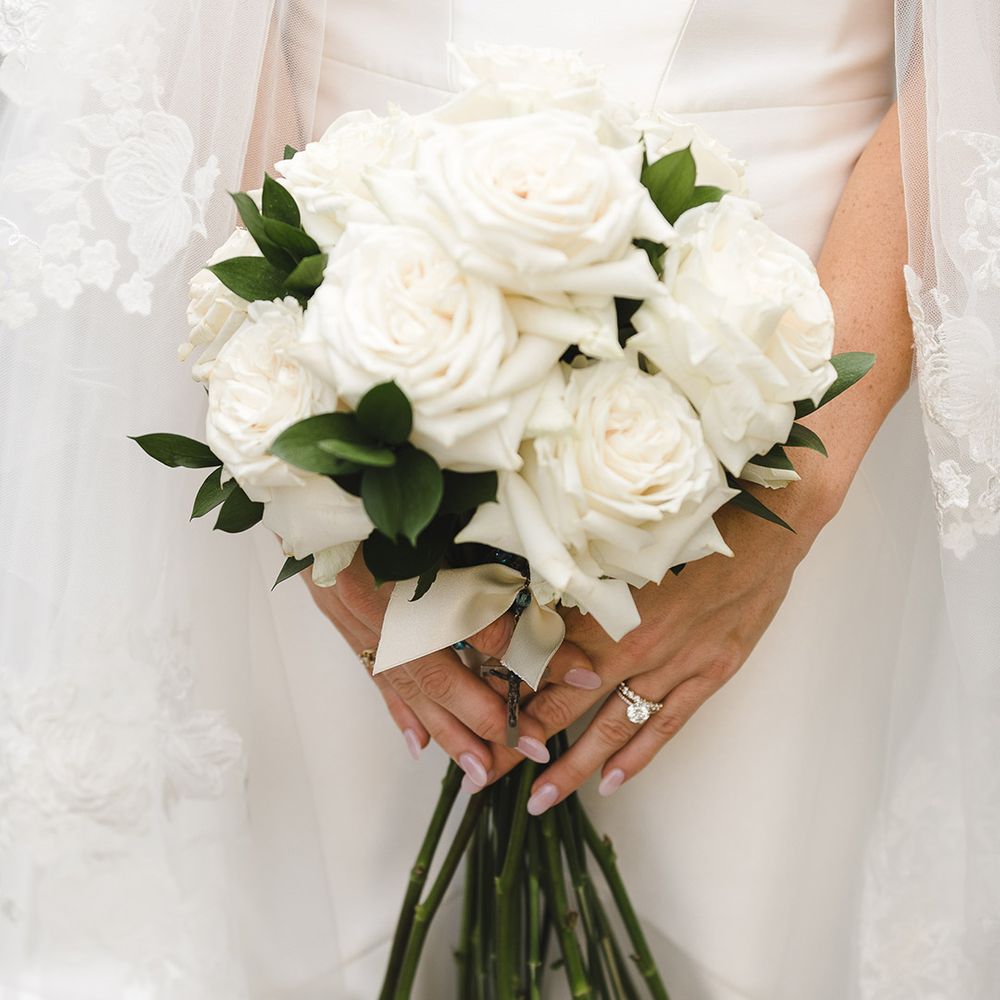 Classic white rose wedding bouquet with long stems worn by bride with rounded pink nails 