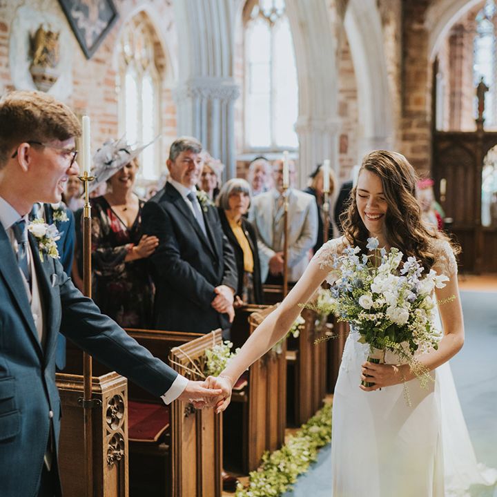 The bride reaches out to hold hands with the groom after walking down the aisle to him for the church wedding 