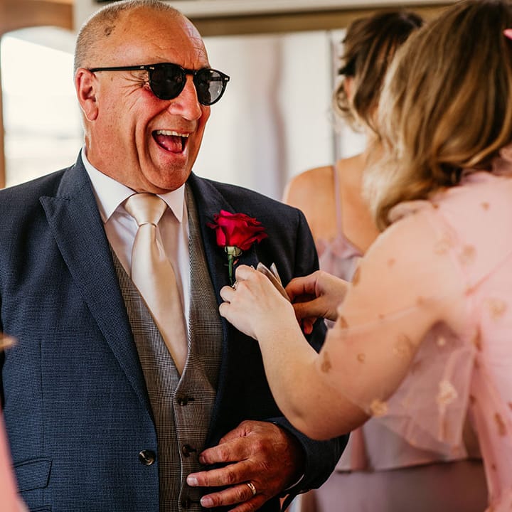 Father of the bride in navy suit with sunglasses and bright pink flower buttonhole 