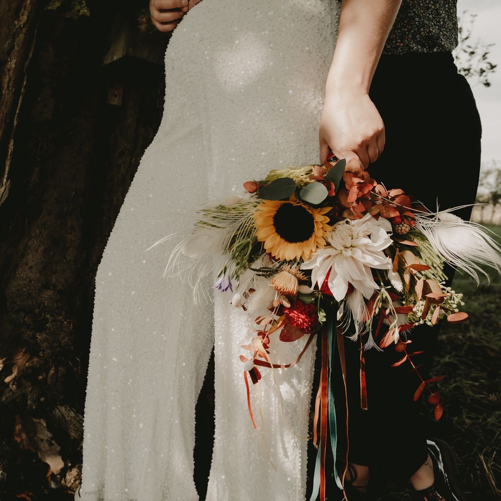 Bride in sequin jumpsuit holding a sunflower bouquet 