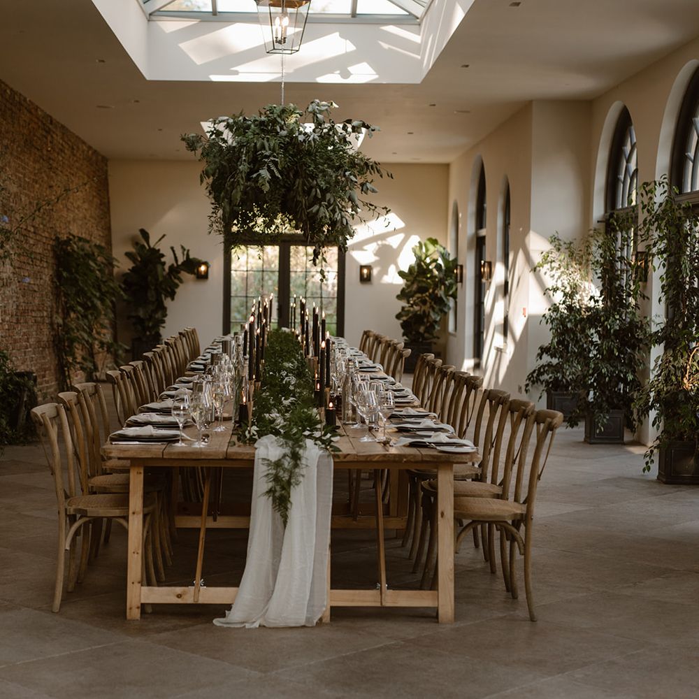 Wooden wedding table with rustic decor, wooden chairs, foliage cloud, greenery and black candles in the Fig House at Middleton Lodge
