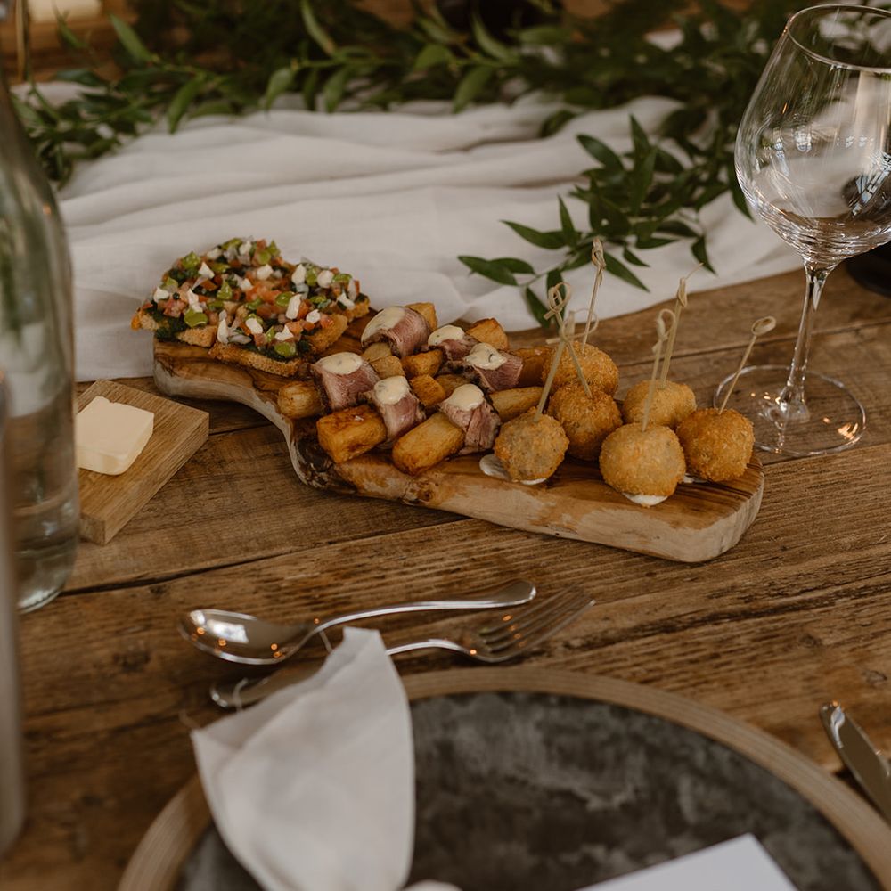 Mediterranean themed platter on wooden board laid at rustic wooden wedding table with, greenery, black candles and tableware